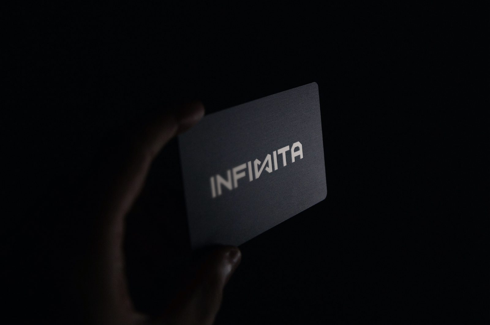 Tarjeta de INFINITA sostenida en mano, sobre fondo oscuro